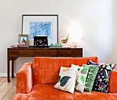 Orange sofa with patterned scatter cushions in front of table lamp on antique console table