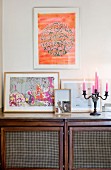 Pink candles in candelabra next to framed pictures on top of retro sideboard