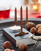 A mini candelabra made from walnut wood with a burning tealight in front of it on a box of matches with nuts as decoration