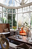 Rustikale Holzmöbel und orangefarbener gepolsterter Sessel in verglastem Wintergarten