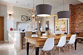 Klassikerstühle mit weisser Sitzschale um Holztisch unter Hängeleuchten mit grauem, konischem Schirm, gegenüber Küchenblock in offener Küche