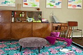 Retro sideboard with glass-fronted top section, framed colourful pictures on wall and patterned turquoise rug in eclectic living area
