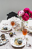 Vintage-style place setting on table with teacups, old cake tins and postcards