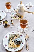 Nostalgisch dekorierter Tisch, Teetassen, Kuchenteller mit alten Backförmchen und Postkarten