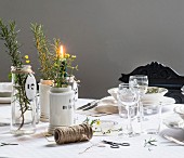 Blumen und Kräuter in Glas- und Porzellanvasen vor Gedeck mit Weingläsern auf Tisch