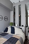 Bett mit Patchworkdecke vor einer grauen Wand mit Sims und Lichtfenstern