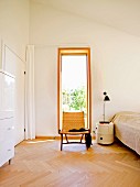 Geflecht Sessel vor Fenster, seitlich zylindrisches Nachtkästchen neben Bett in minimalistischem Schlafzimmer