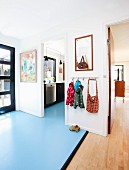 Hallway with wooden flooring and pale blue lino flooring, children's coat rack and open doorway leading into kitchen
