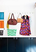 Leather bags and patterned tunic hung from wall hooks above cupboards with black fronts