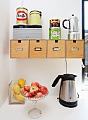 Glass bowls of peaches and lemons next to kettle below wooden boxes in wall-mounted bracket with tin can and coffee maker on top