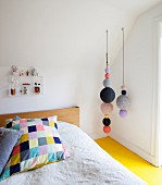 Colourful patchwork pillow on bed, various knitted balls hung from sloping ceiling and yellow-painted wooden floor