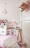 Open door decorated with fabric hunting trophy, round rag rug, pink wooden floor and white furniture in child's bedroom