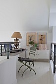 Study on white gallery level with pastel green vintage garden chair, antique table lamp and metal sideboard
