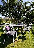 Wooden table and white chairs made from curved metal in summery garden