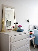 Make-up brushes and framed mirror on chest of drawers next to three-legged stool and bed in bedroom