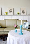 Cottage ambiance; round table, antique sofa in front of white-painted wainscoting with framed drawings on top