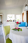Chair with pale green upholstery at table with white tablecloth and flower arrangements in cottage interior