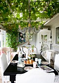 Black-painted table and white chairs on veranda below climber-covered pergola