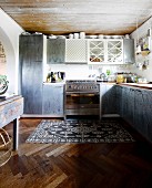 Fitted kitchen with grey mottled doors in simple kitchen with vintage rug on herringbone floor