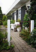 Offenes Gartentor und gepflasterter Weg entlang eines Wohnhauses, davor weiße Sitzbank