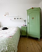 Bäuerlicher Eckschrank grün lackiert, neben Nachtkästchen und Doppelbett mit Katze auf Tagesdecke
