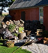 Metal outdoor armchairs and fire bowl on terrace with campfire bread over fire and firewood stacked against house