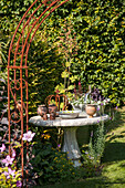 View through rusty trellis arch to garden ornaments on stone table in antique Greek style