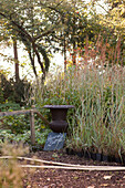 Urn and handwritten sign in front of grasses in plant nursery