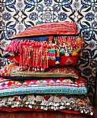Bunt gewebte Kissen mit Perlenfransen und Pailletten vor floral gemusterten, marokkanischen Wandfliesen