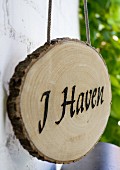 Slice of tree trunk with burnt lettering reading 'I Haven' hanging from cord