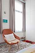 Brown leather easy chair on flokati rug between windows with pale grey curtains