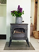 Bouquet of lilac in zinc pot on top of vintage, log-burning stove