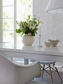 Romantic arrangement of lit candle and vase of flowers on glossy white table in front of open terrace doors