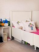 Girl's bedroom with white, extendible bed, scatter cushions and retro-style bedside table