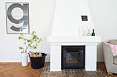 Open fireplace, logs in bucket and white vase of leafy branches below framed typographical poster
