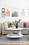 Round side table in front of grey sofa on rug with retro pattern; framed pictures on wall