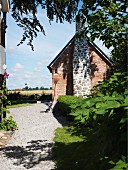 Sunny gravel garden path leading to simple brick house with external chimney