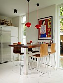 Counter with stainless steel base, bar stools with wooden shell seats, red pendant lamps and French windows to one side