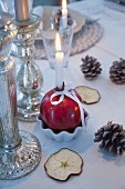 Lit candle in pomegranate used as candlestick, pine cones and dried sliced of apple on table with white táblecloth