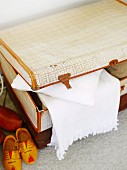 Pale vintage suitcase, white blanket and wooden clogs arranged on carpeted floor