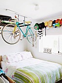 Racing bicycle hung from shelf above bed in teenager's bedroom with collection of peaked hats on wall