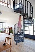 Woman walking up cast-iron spiral staircase in open-plan interior