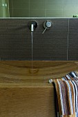 Eleganter Holzwaschtisch mit eingearbeitetem Waschbecken und gestreiftem Handtuch, Wandarmatur mit Wasserstrahl
