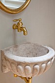 Shell-shaped stone sink below brass, wall-mounted tap