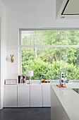 weiße Küchenunterschränke vor Fenster mit Gartenblick
