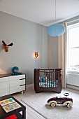White retro chest of drawers, dark brown modern cot and ride-on toy car in nursery