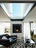 Black leather armchair and coffee table in front of fireplace in living room with large skylight