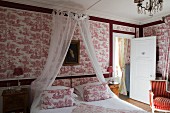Double bed with canopy against red and white toile de jouy wallpaper