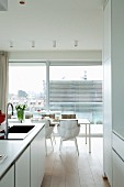Blick von offener Küche auf hellen Esstisch mit Designerstühlen vor Fensterfront