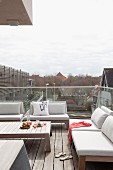 Roof terrace with glass balustrade, outdoor furniture with pale cushions and coffee table